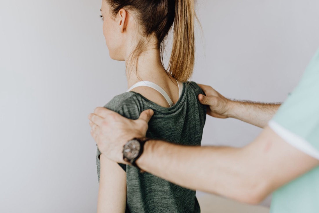 Physiotherapeut legt die Hände auf die Schultern einer Patientin